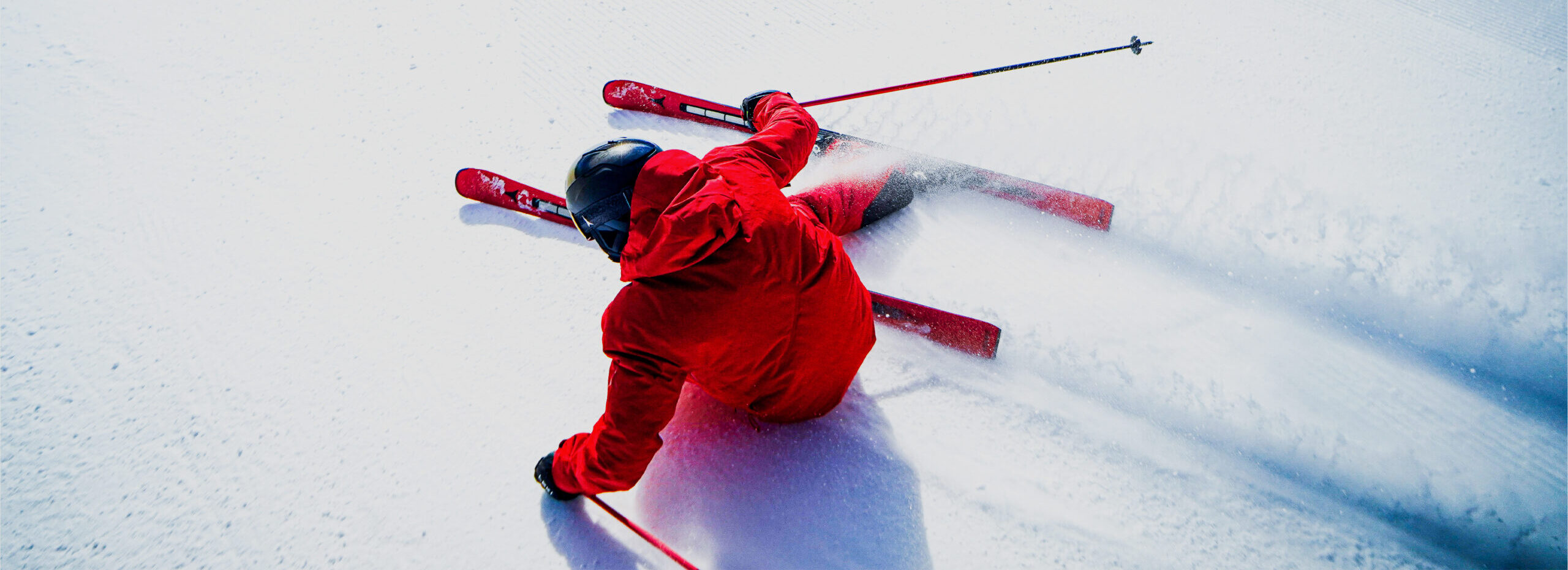 Rear view of skier in red suit skiing straight down an overexposed snowy hill.