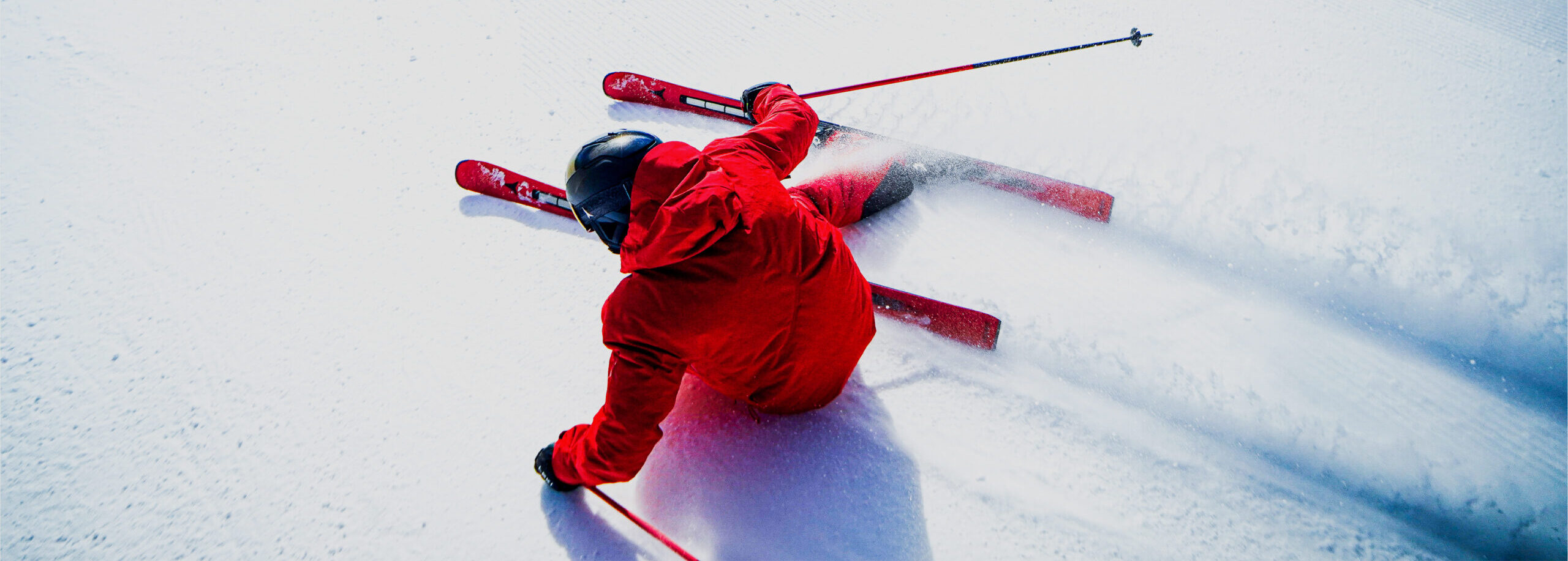 Rear view of skier in red suit skiing straight down an overexposed snowy hill.